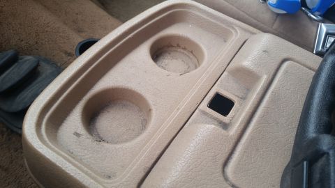 1985 Ford Bronco - Close-up of the interior center console, showing the cup holder area and a small cubby.