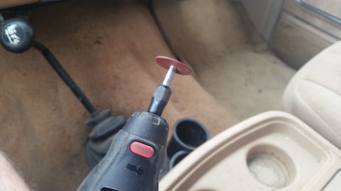 1985 Ford Bronco - A rotary tool is positioned near the gear shifter inside a vehicle's interior, with a cup holder visible.