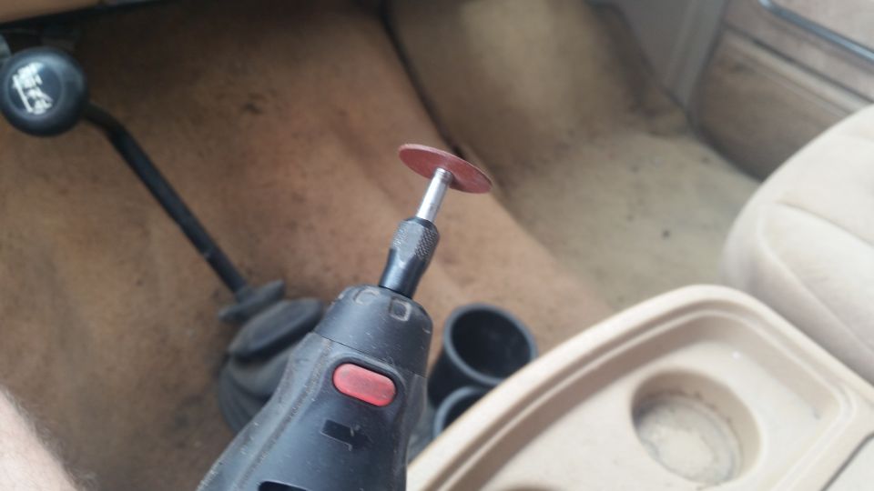 Rotary tool with cutting disc near a 4-speed gear shifter in a tan interior. The cup holder is visible