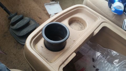 1985 Ford Bronco - Interior view of a tan center console with cup holders and a gear shifter boot, likely from a vehicle in the 1980s.