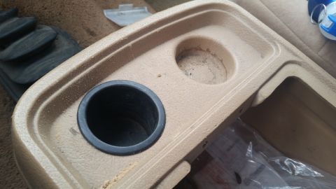 1985 Ford Bronco - Interior view of a tan center console two cup holders and a storage area.