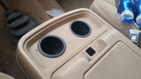 1985 Ford Bronco - Interior shot of a vehicle's center console showing cup holders and gear shifter boot.