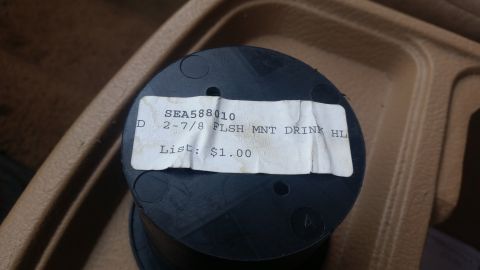 1985 Ford Bronco - A close-up view of a black plastic cup holder part with a label indicating its part number and price.