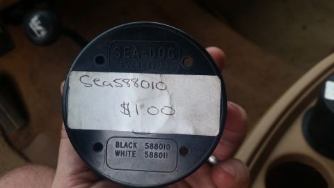 1985 Ford Bronco - A black Sea-Dog cup holder part is held in hand, showing a handwritten label with a part number and price of $1.00.