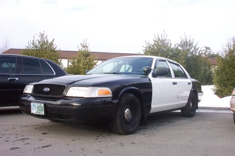 2001 Ford Crown Victoria - A two-tone Ford Crown Victoria police car is parked next to another dark sedan.