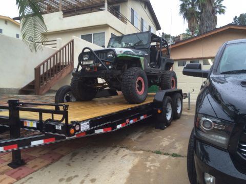 1992 Jeep Wrangler - A lifted Jeep Wrangler is loaded onto a trailer, parked next to a modern pickup truck.