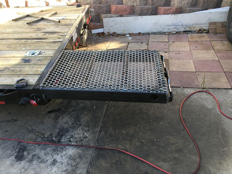Flatbed trailer with wooden deck and metal ramp, seen from the rear