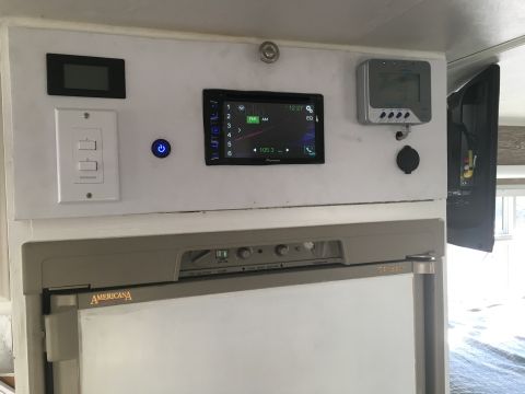 1992 Jeep Wrangler - Close-up of an RV's control panel a stereo, digital displays, and a refrigerator unit labeled Americana above a refrigerator.