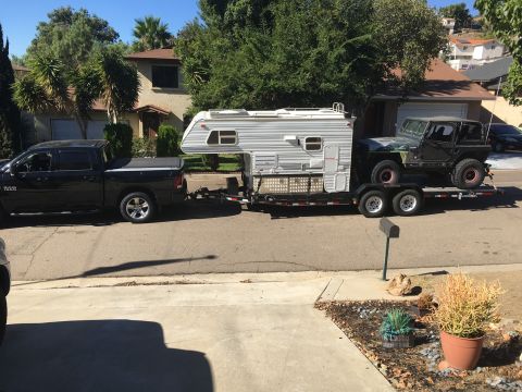 1992 Jeep Wrangler - A 1992 Jeep Wrangler is transported on a trailer behind a black pickup truck, loaded with a camper shell.