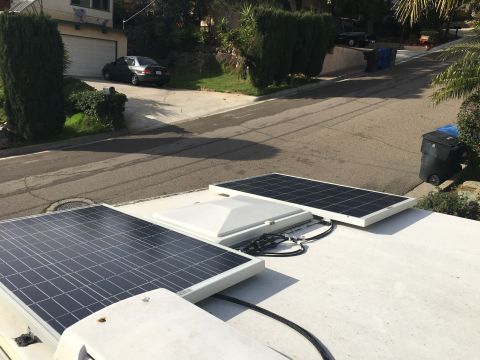 1992 Jeep Wrangler - Solar panels are installed on the roof of a structure, with a dark sedan visible in the driveway.