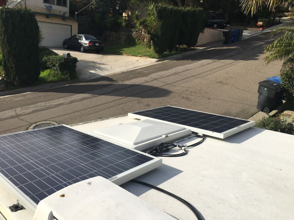 Solar panels on a white roof with a dark sedan parked in a driveway in the background
