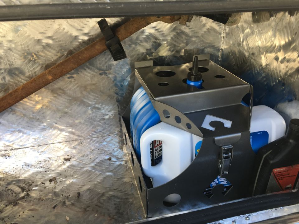 Metal tool organizer holding bottles of fluid and a rusty bar, inside a metal compartment
