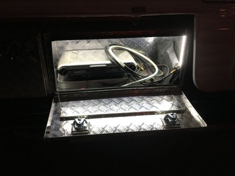 1992 Jeep Wrangler - An open storage compartment reveals a portable stove and coiled cables, illuminated by interior lights.