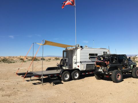 1992 Jeep Wrangler - A heavily modified Jeep Wrangler sits in the desert next to a trailer, with a Confederate flag flying high above.