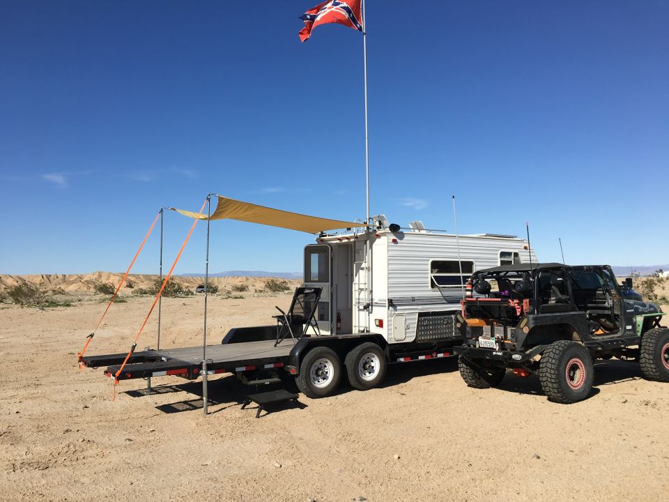 Modified black Jeep Wrangler parked in desert with trailer and Confederate flag