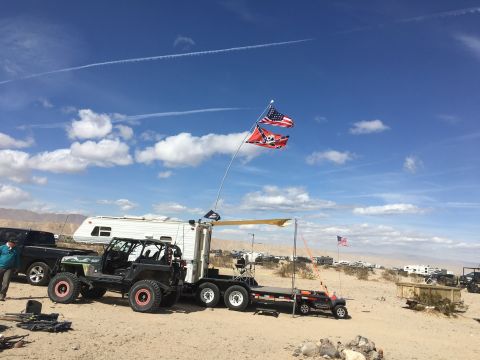 1992 Jeep Wrangler - A modified off-road vehicle is parked on a trailer in a desert setting, with several RVs and other vehicles visible in the distance.
