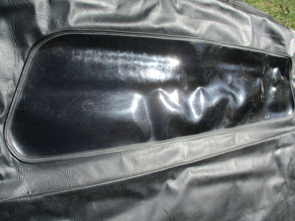 Close-up of a black soft top with a clear plastic window. The window is wrinkled and scratched