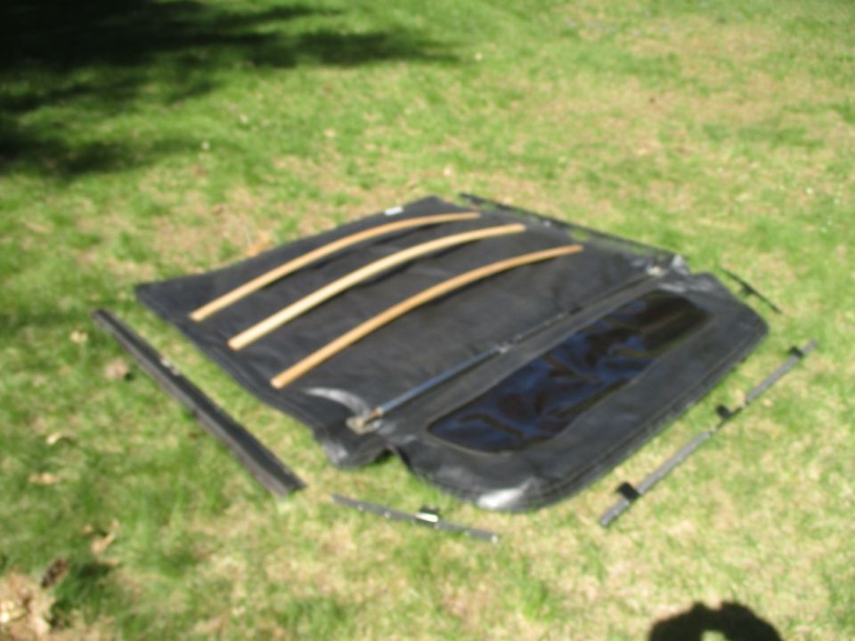 Black soft top with wooden support bars lying on grass