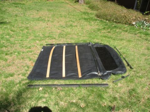 1996 Ford Bronco - A disassembled soft top, likely for a convertible or SUV, lies spread out on a grassy lawn with its supporting frame pieces nearby.
