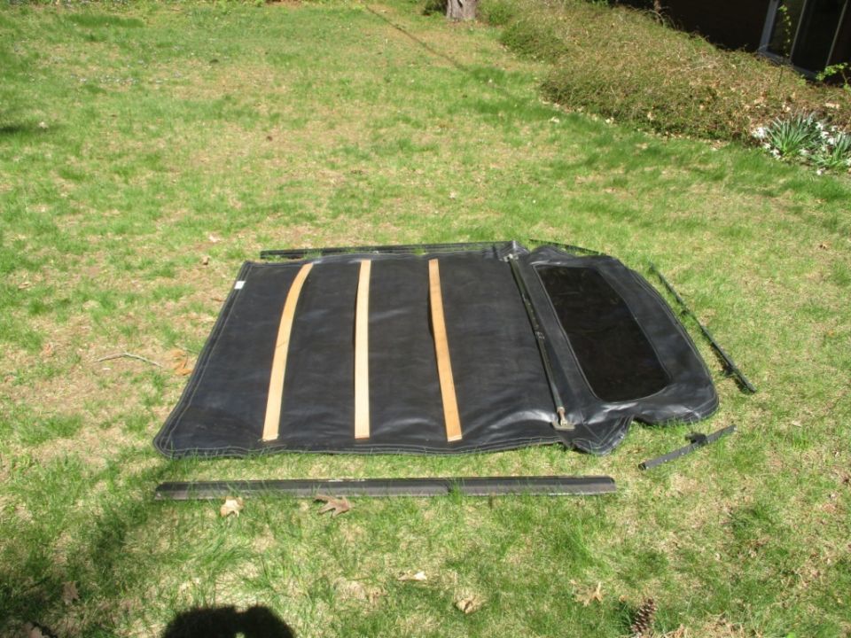 Disassembled black soft top with wooden support slats and metal trim pieces on grass