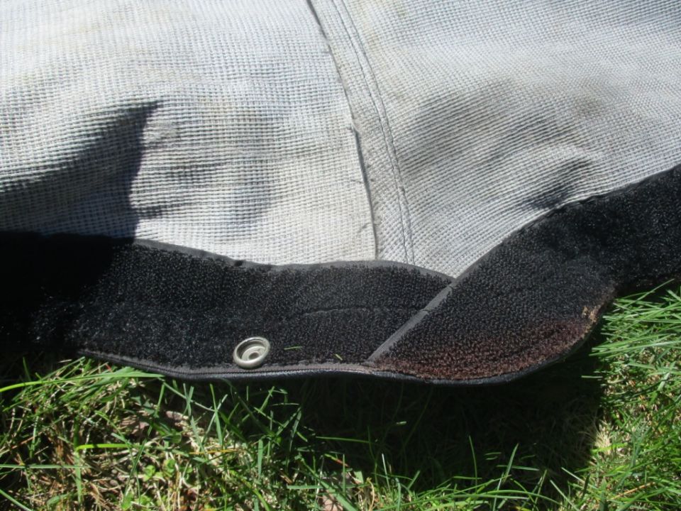 Close-up of a car cover's velcro strap and grommet on grass