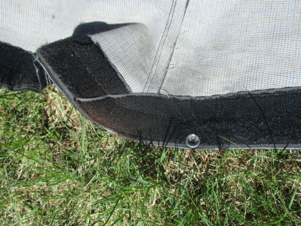 Close-up of a car cover's edge with velcro and a grommet, resting on grass