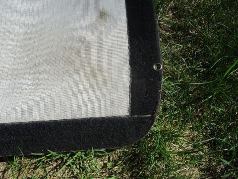 1996 Ford Bronco - Close-up of a white soft top corner with black trim and a metal grommet, resting on green grass.