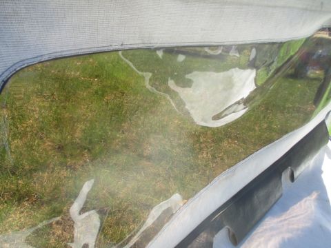 1996 Ford Bronco - Close-up of a vehicle's soft top window, revealing the grassy area beyond.