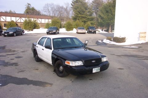 2001 Ford Crown Victoria - A two-tone police car, likely a 2001 Ford Crown Victoria, is parked in a lot with other vehicles visible in the background.