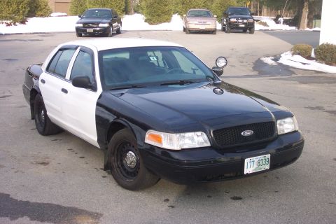 2001 Ford Crown Victoria - Two-tone police Crown Victoria parked outside with other cars visible in the background.