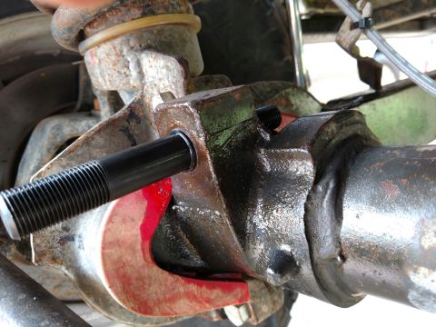 1992 Ford Bronco - A mechanic works on a vehicle's suspension system, focusing on a bolt insertion into a bracket.