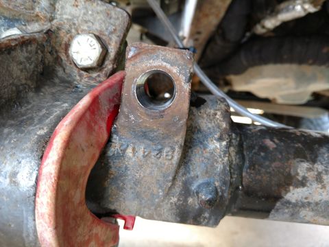 1992 Ford Bronco - Close-up of a rusty bracket with a bolt and red clamp, showing some stamped numbers.