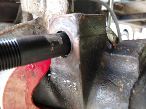 1992 Ford Bronco - A close-up view of a vehicle's suspension part, showing a bolt being inserted into a hole.