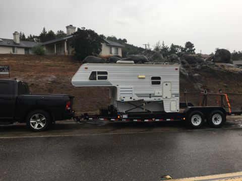 1992 Jeep Wrangler - A black pickup truck tows a white camper on a trailer down a wet road.
