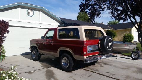 1985 Ford Bronco - Rear view of a red and tan 1985 Ford Bronco with a spare tire mounted on the tailgate.