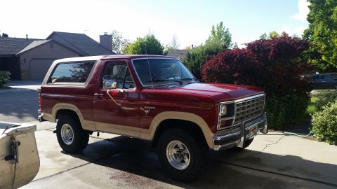1985 Ford Bronco - A red and tan Ford Bronco is parked in a residential driveway on a sunny day.