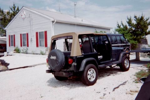 1992 Jeep Wrangler - A black Jeep Wrangler is parked on a gravel driveway in front of a white house with red shutters.