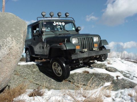 1992 Jeep Wrangler - A green Jeep Wrangler navigates a rocky, snow-covered terrain under a partly cloudy sky.