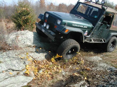 1992 Jeep Wrangler - A Jeep Wrangler navigates a rocky off-road course with autumn foliage on the ground.