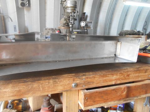 1992 Ford Bronco - Metal part resting on a workbench in a workshop setting with machinery visible.