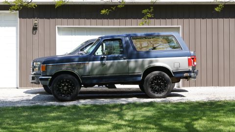 1987 Ford Bronco - Side view of a blue and gray 1987 Ford Bronco with aftermarket wheels.