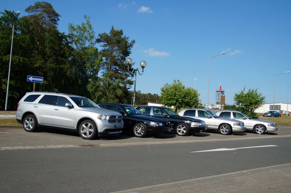 Silver SUV and several sedans parked in a lot under a blue sky