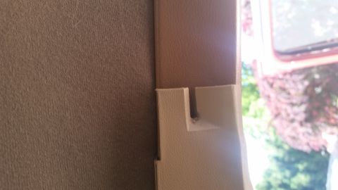 1985 Ford Bronco - A close-up view shows the interior trim of a vehicle, specifically a beige plastic piece with a small notch, adjacent to a textured brown f…