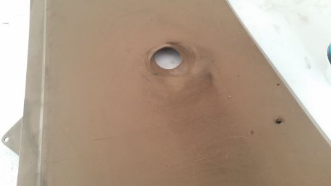 1985 Ford Bronco - A close-up view of a tan interior panel with a circular cutout and a smaller hole for a fastener. The panel shows some scuff marks and dust.