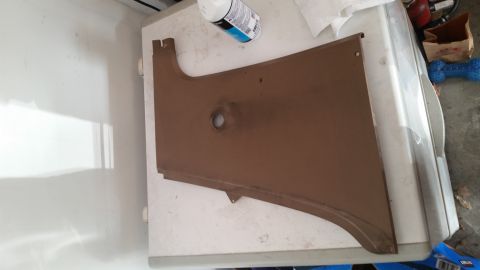1985 Ford Bronco - A brown, curved metal panel with a central circular cutout rests on a white surface, possibly a refrigerator. The panel appears to be a veh…