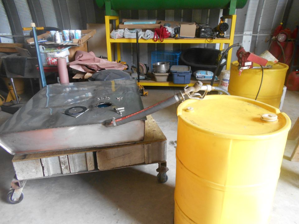 Metal fuel tank on cart with hose connected to red fuel pump and yellow barrel