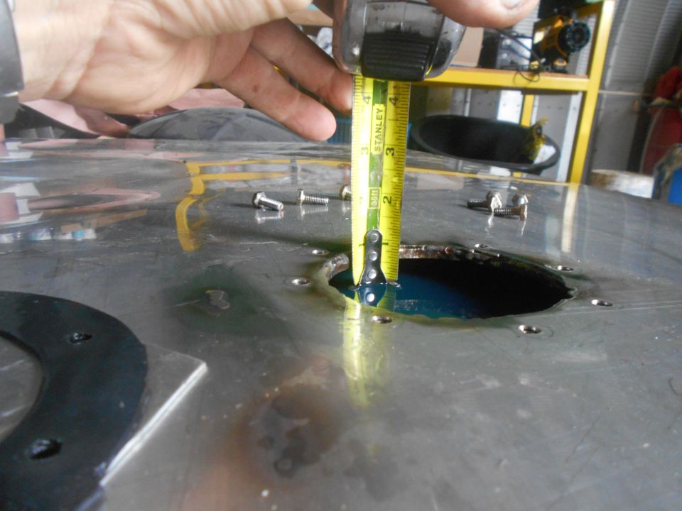 Measuring depth of blue liquid in a circular opening on a metal surface with a tape measure.