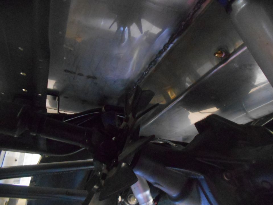 Underside of vehicle showing drivetrain, differential, driveshaft, and fan.