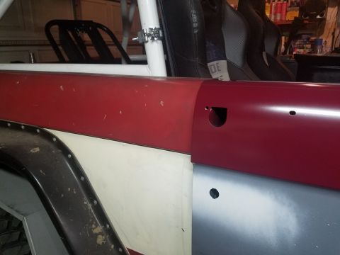 1968 Ford Bronco - A close-up view of the side of a vehicle, showing a red upper body panel and a gray lower body panel. Visible modifications include a roll…