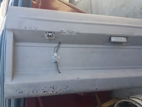 1968 Ford Bronco - A close-up view of a light gray vehicle door or tailgate with a white handle and a visible electrical wire attached to a metal bracket.